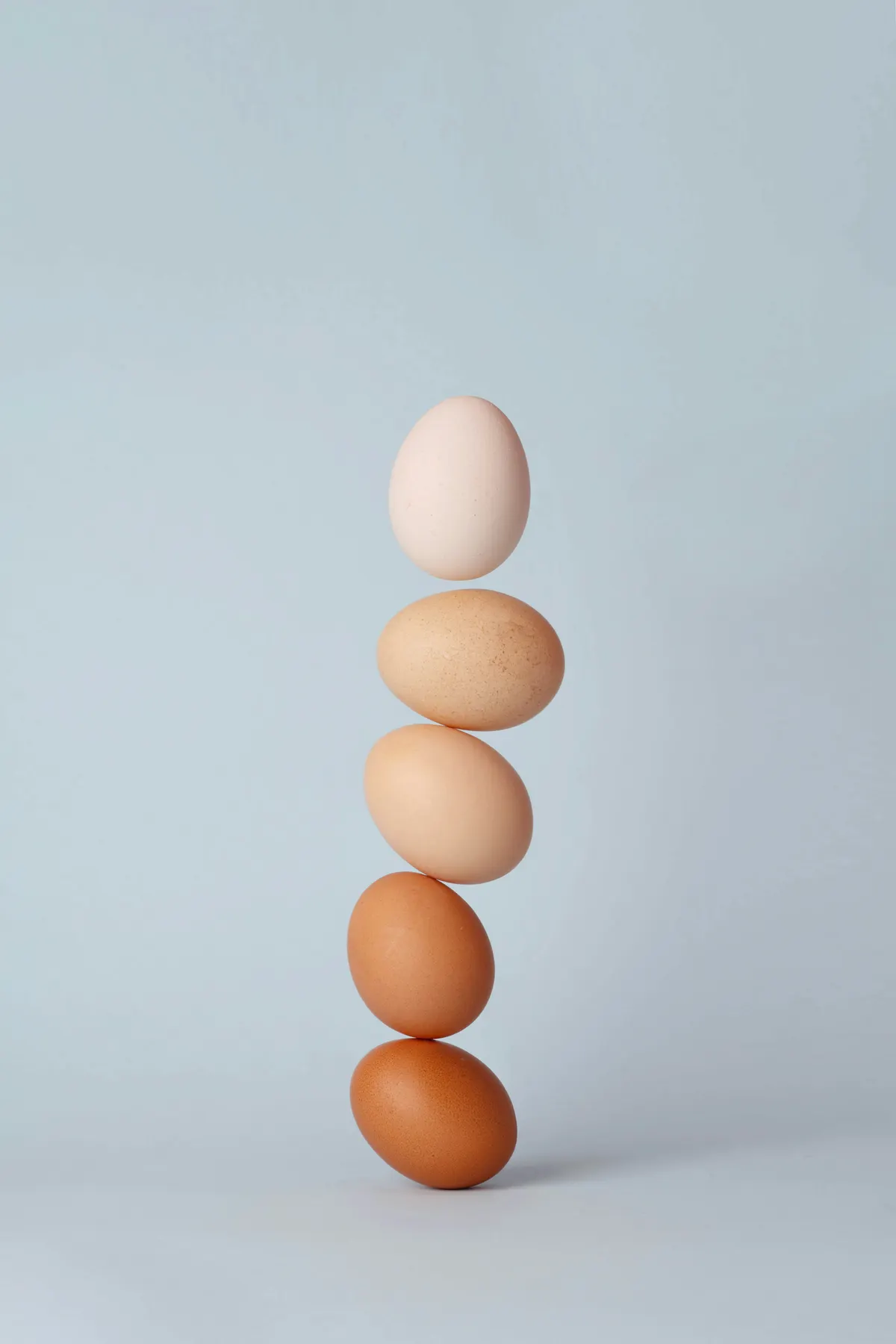 Huevos de distintos tonos apilados en equilibrio, uno sobre otro, con fondo celeste